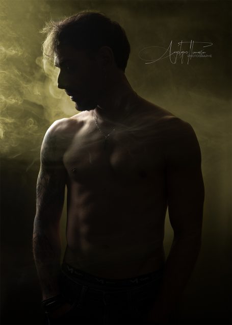 Homme/Femme/Boudoir Homme torse nu en silhouette, entouré de fumée dans une lumière tamisée.